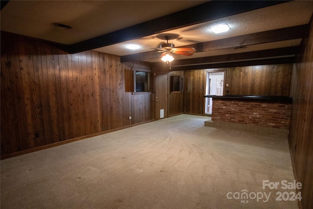 unfurnished living room featuring carpet, beam ceiling, wood walls, and ceiling fan