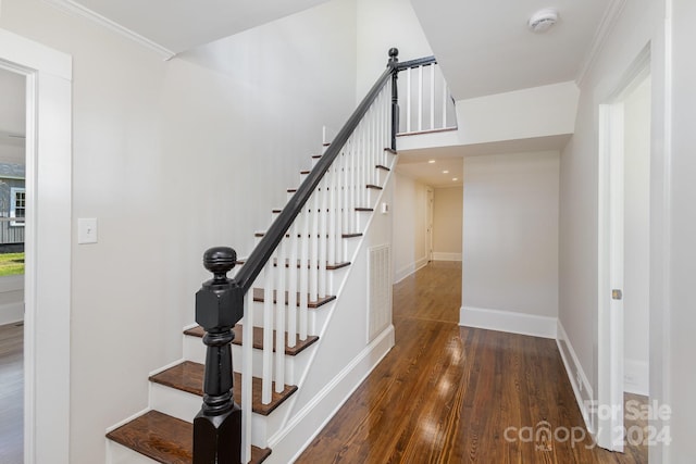 stairway with dark wood-type flooring and ornamental molding