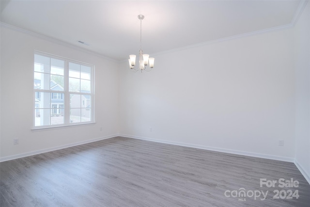 spare room with wood-type flooring, an inviting chandelier, and crown molding