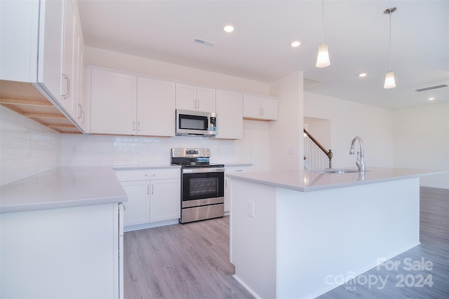 kitchen with appliances with stainless steel finishes, a kitchen island with sink, light wood-type flooring, and white cabinetry