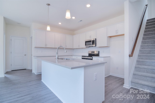 kitchen with appliances with stainless steel finishes, light wood-type flooring, sink, and a center island with sink