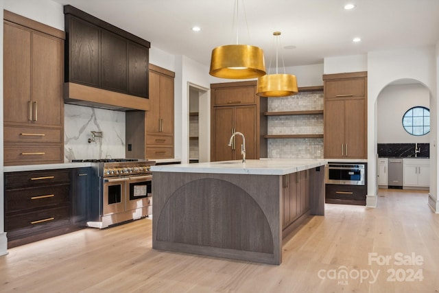 kitchen with backsplash, a center island with sink, stainless steel appliances, and light wood-type flooring