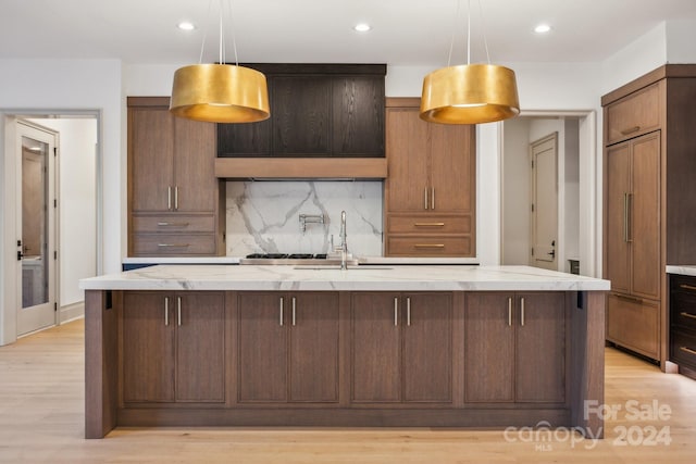 kitchen featuring tasteful backsplash, light stone counters, a spacious island, decorative light fixtures, and light hardwood / wood-style floors