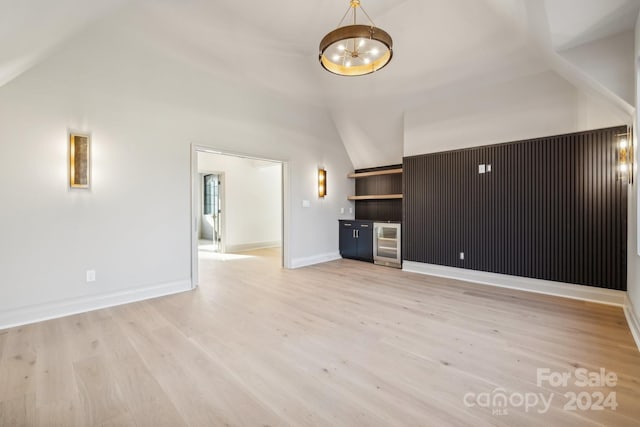 unfurnished living room featuring light wood-type flooring, beverage cooler, and lofted ceiling