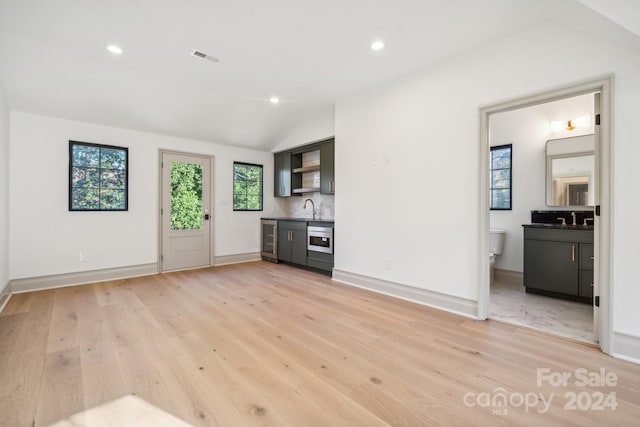 unfurnished living room featuring light hardwood / wood-style floors, lofted ceiling, and sink