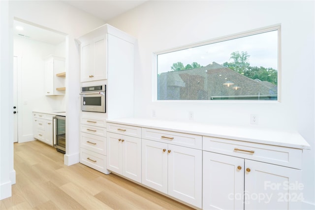 kitchen with white cabinets, oven, light wood-type flooring, and beverage cooler