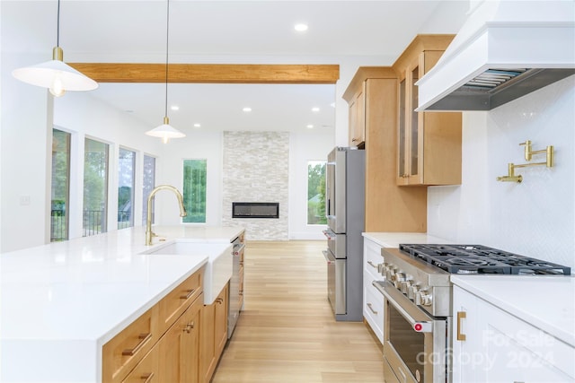 kitchen with appliances with stainless steel finishes, custom range hood, pendant lighting, beam ceiling, and a stone fireplace