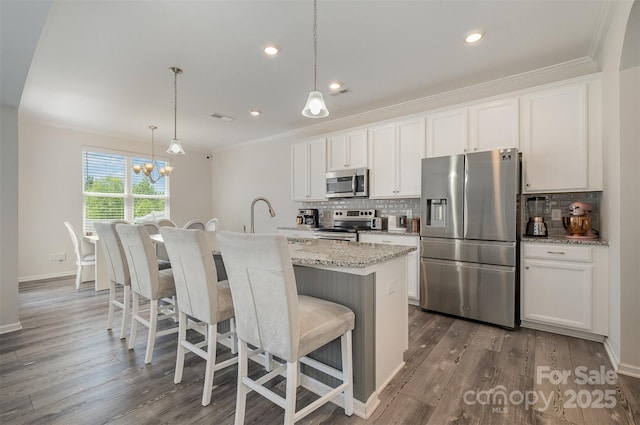 kitchen with stainless steel appliances, hanging light fixtures, a center island with sink, and white cabinets