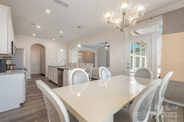 dining area featuring dark hardwood / wood-style flooring, sink, crown molding, and ceiling fan with notable chandelier