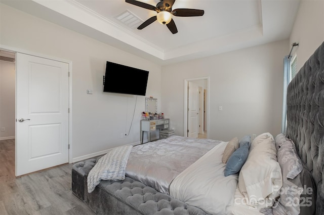 bedroom featuring ceiling fan, a raised ceiling, and light wood-type flooring