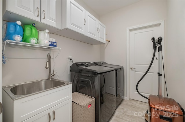 clothes washing area featuring cabinets, sink, washing machine and dryer, and light hardwood / wood-style flooring