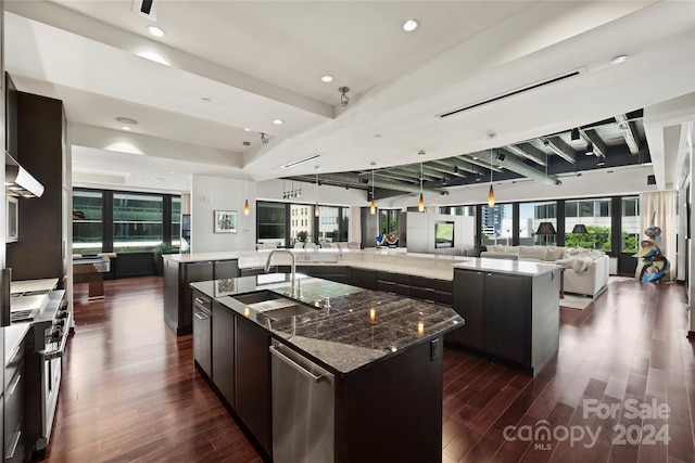 kitchen with dark brown cabinetry, sink, wall chimney range hood, a spacious island, and dark hardwood / wood-style floors