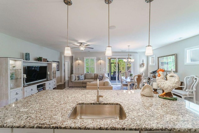 kitchen with a center island with sink, sink, hanging light fixtures, light stone countertops, and ceiling fan with notable chandelier