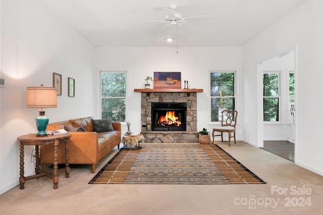 carpeted living room with a stone fireplace, ceiling fan, and plenty of natural light