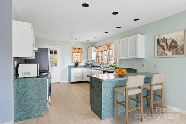 kitchen with kitchen peninsula, sink, ceiling fan, a breakfast bar area, and white cabinets