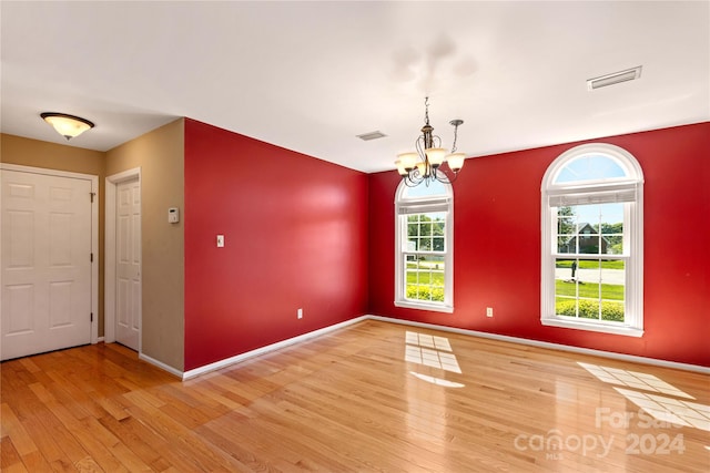 spare room featuring wood-type flooring, plenty of natural light, and an inviting chandelier