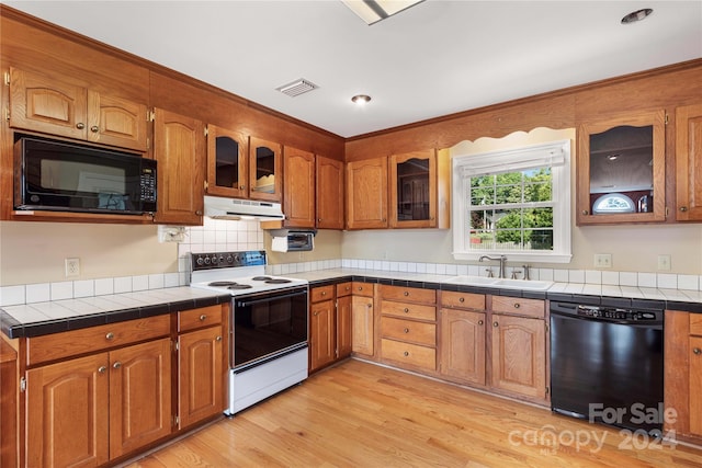 kitchen featuring light hardwood / wood-style flooring, black appliances, sink, tasteful backsplash, and tile countertops