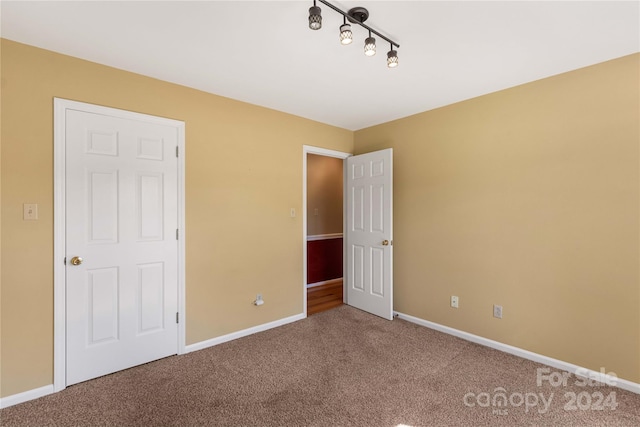 unfurnished bedroom featuring rail lighting and carpet