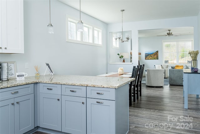 kitchen featuring decorative light fixtures, ceiling fan with notable chandelier, dark wood-type flooring, kitchen peninsula, and light stone counters