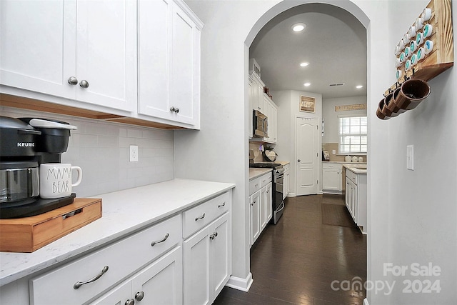 kitchen featuring appliances with stainless steel finishes, tasteful backsplash, white cabinetry, dark hardwood / wood-style flooring, and light stone countertops