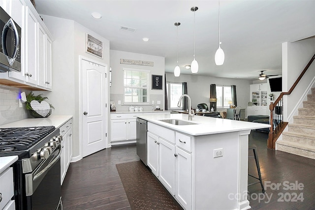 kitchen featuring appliances with stainless steel finishes, hanging light fixtures, ceiling fan, dark hardwood / wood-style floors, and an island with sink