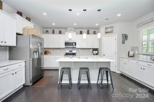 kitchen featuring hanging light fixtures, appliances with stainless steel finishes, a kitchen island with sink, and dark wood-type flooring