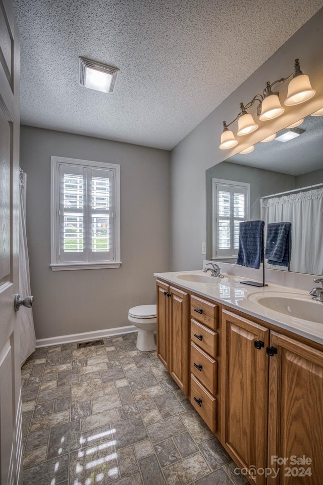 bathroom with dual sinks, vanity with extensive cabinet space, toilet, and a wealth of natural light