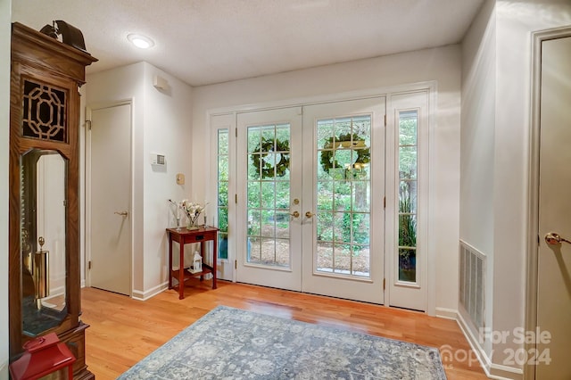 entryway featuring light wood-type flooring, french doors, and a textured ceiling