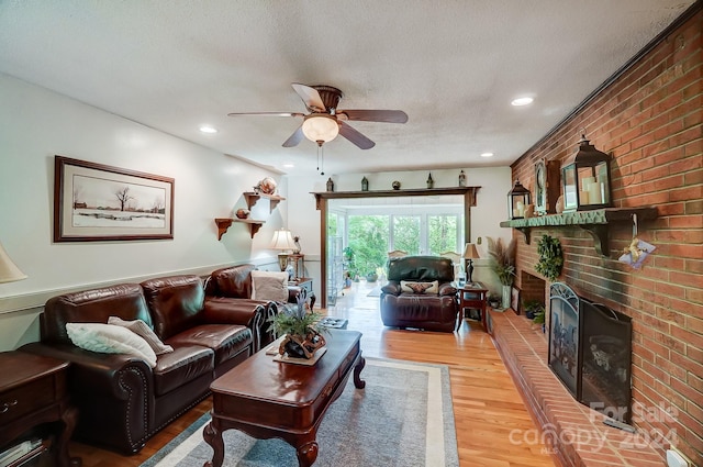 living room featuring a fireplace, ceiling fan, brick wall, light hardwood / wood-style flooring, and a textured ceiling