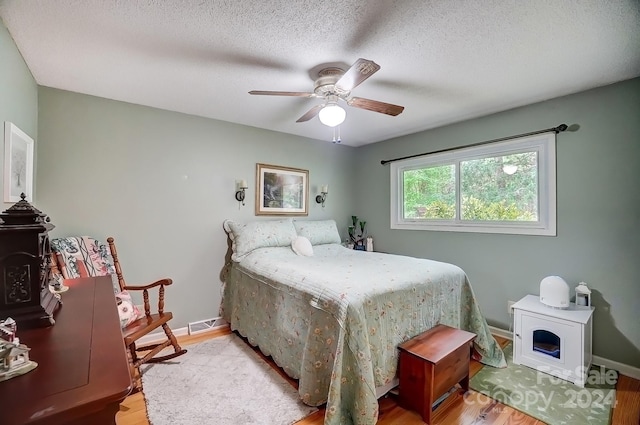 bedroom featuring a wood stove, a textured ceiling, light wood-type flooring, and ceiling fan