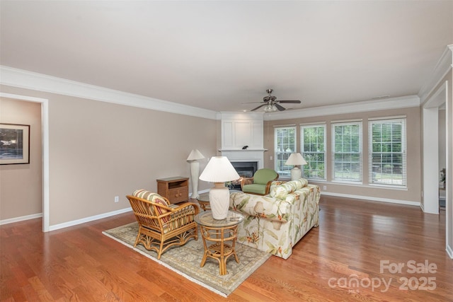 living room featuring ceiling fan, a large fireplace, ornamental molding, and wood-type flooring