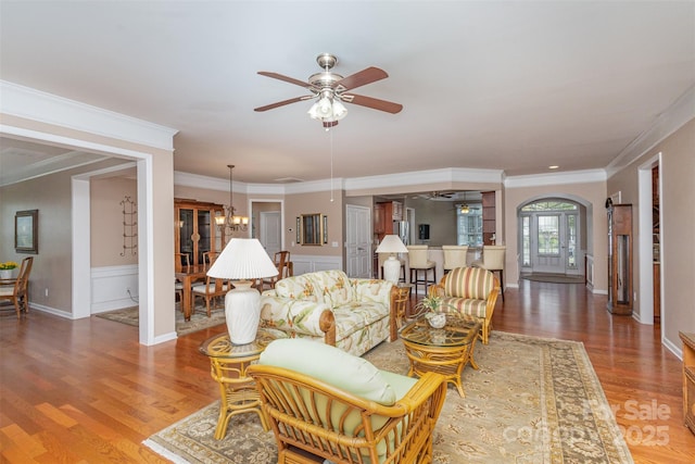 living room featuring wood-type flooring, ceiling fan with notable chandelier, and crown molding