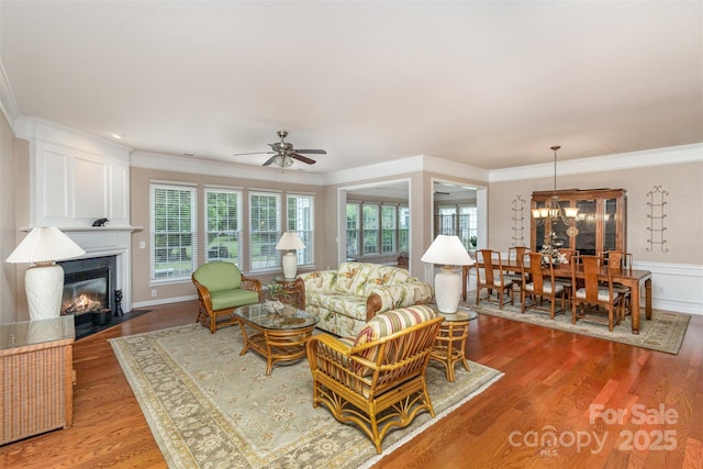 living room with ceiling fan with notable chandelier, wood-type flooring, and ornamental molding