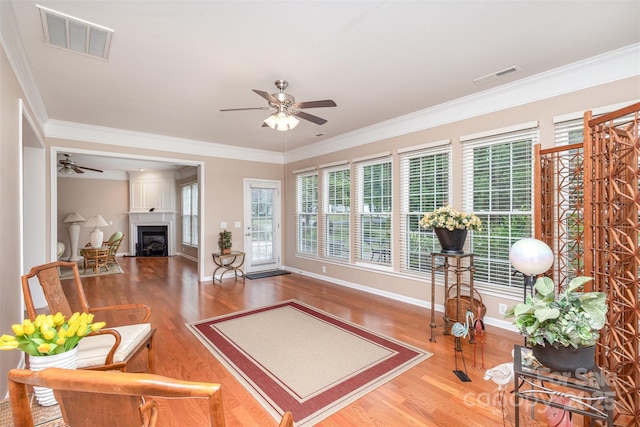 living room with crown molding, a large fireplace, ceiling fan, and hardwood / wood-style floors