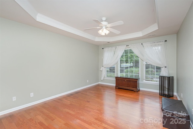 empty room featuring ceiling fan, ornamental molding, a tray ceiling, and light hardwood / wood-style floors