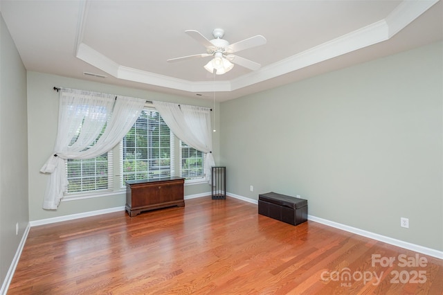 empty room featuring a raised ceiling, wood-type flooring, ceiling fan, and crown molding