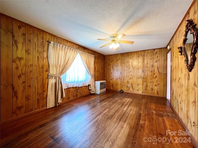 spare room with dark hardwood / wood-style flooring, ceiling fan, wooden walls, and heating unit