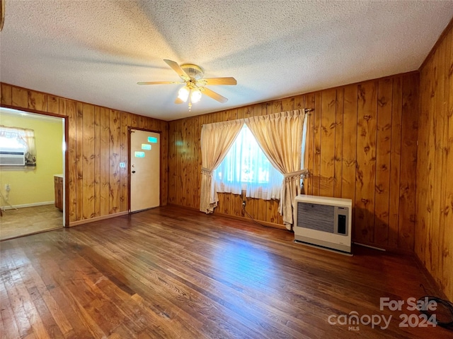 unfurnished living room featuring heating unit, ceiling fan, wood walls, and dark hardwood / wood-style floors