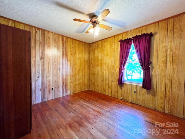 empty room with wood walls, hardwood / wood-style floors, ceiling fan, and a textured ceiling