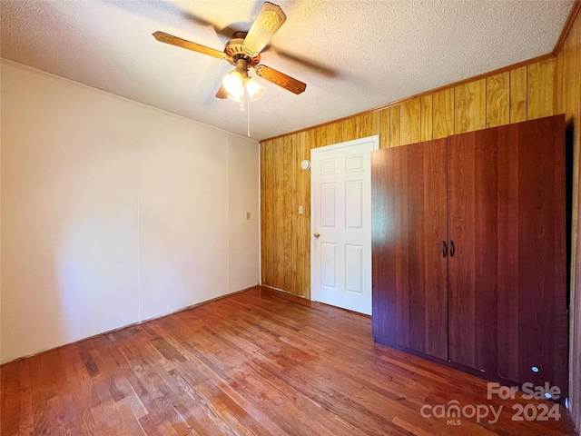 unfurnished bedroom featuring ceiling fan, wood walls, dark hardwood / wood-style floors, and a textured ceiling