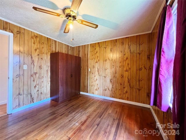 spare room featuring wood-type flooring, a textured ceiling, wooden walls, and ornamental molding