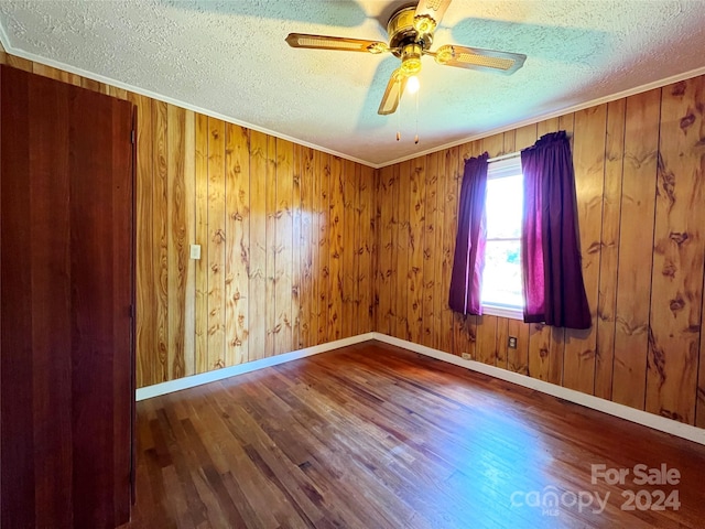 unfurnished room featuring wood walls, hardwood / wood-style floors, a textured ceiling, and ornamental molding