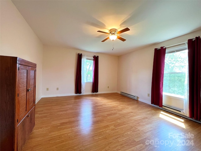 empty room featuring ceiling fan, plenty of natural light, light hardwood / wood-style floors, and a baseboard heating unit