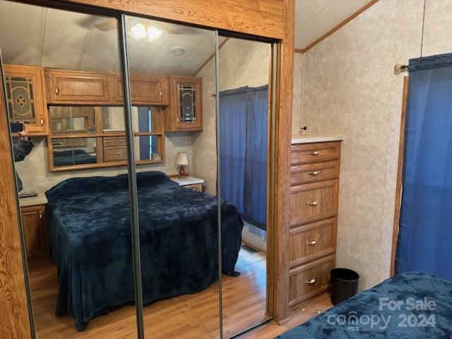 bedroom with a closet, light hardwood / wood-style flooring, lofted ceiling, and crown molding