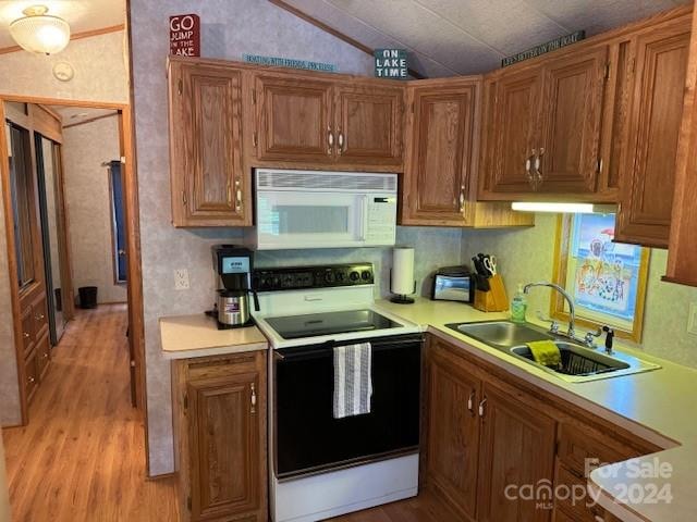 kitchen with white appliances, vaulted ceiling, light hardwood / wood-style floors, and sink