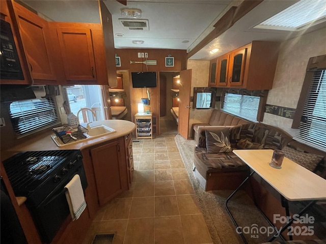 kitchen featuring black stove, a sink, glass insert cabinets, and brown cabinets