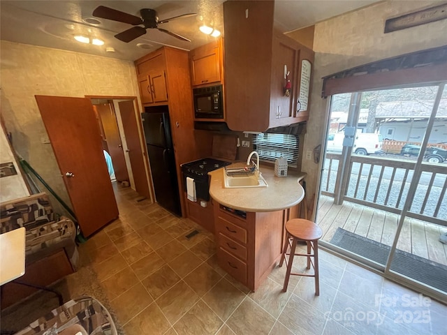 kitchen featuring a breakfast bar area, a sink, light countertops, black appliances, and brown cabinetry