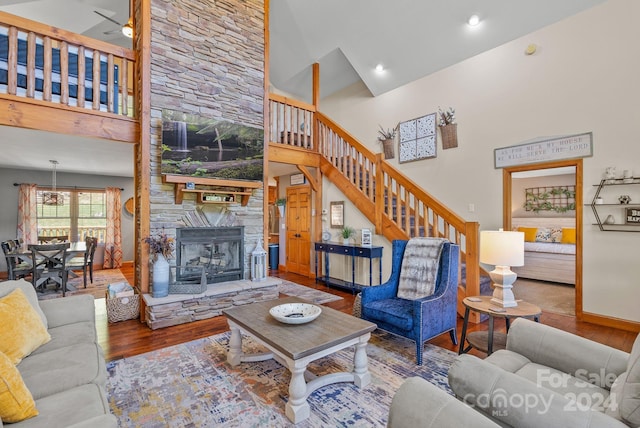 living room featuring high vaulted ceiling, ceiling fan, hardwood / wood-style flooring, and a stone fireplace