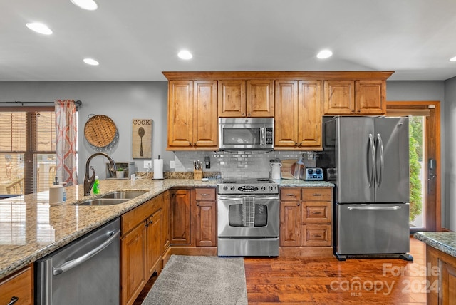 kitchen featuring tasteful backsplash, hardwood / wood-style floors, light stone countertops, appliances with stainless steel finishes, and sink