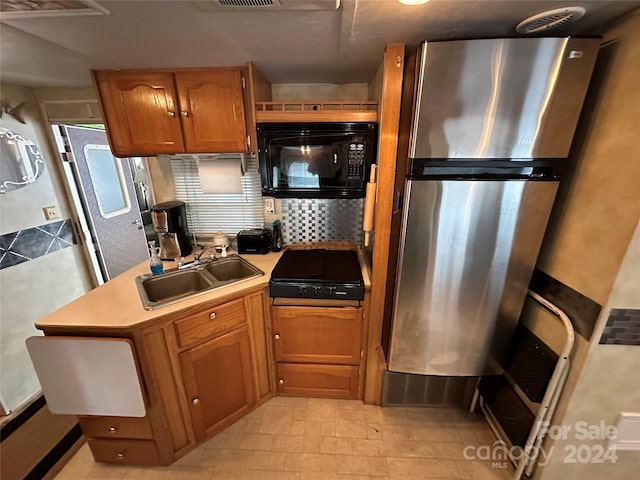 kitchen featuring light tile floors, sink, stainless steel refrigerator, tasteful backsplash, and stovetop